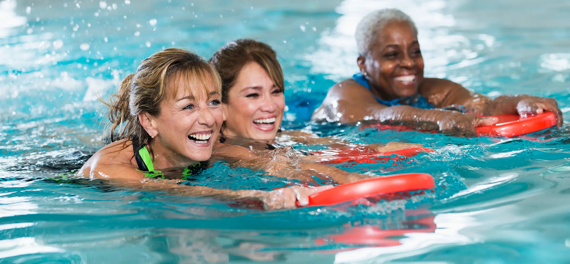 three adult women swimming by holding kick boards