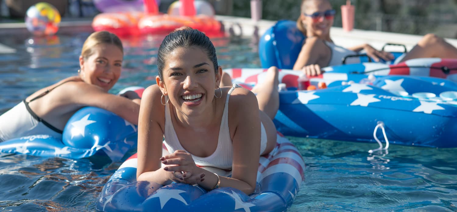 three women with patriotic inflatables in a pool smiling facing the camera