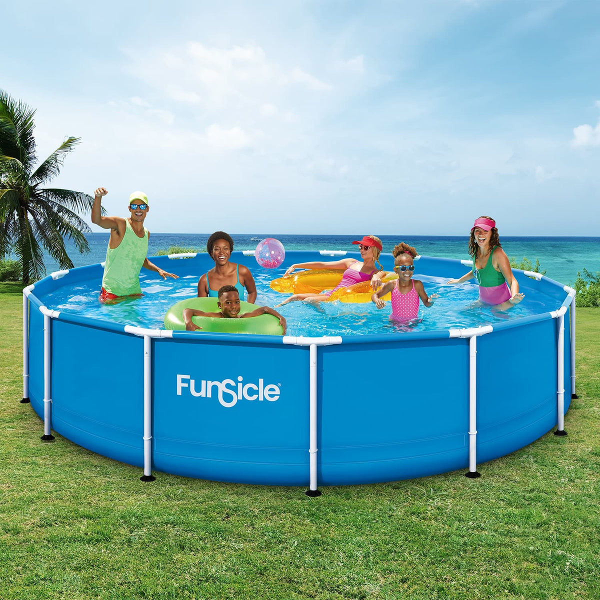 Six people enjoy swimming and playing with colorful inflatable pool floats and beach balls in a blue Funsicle Activity Pool on a grassy lawn overlooking the ocean.