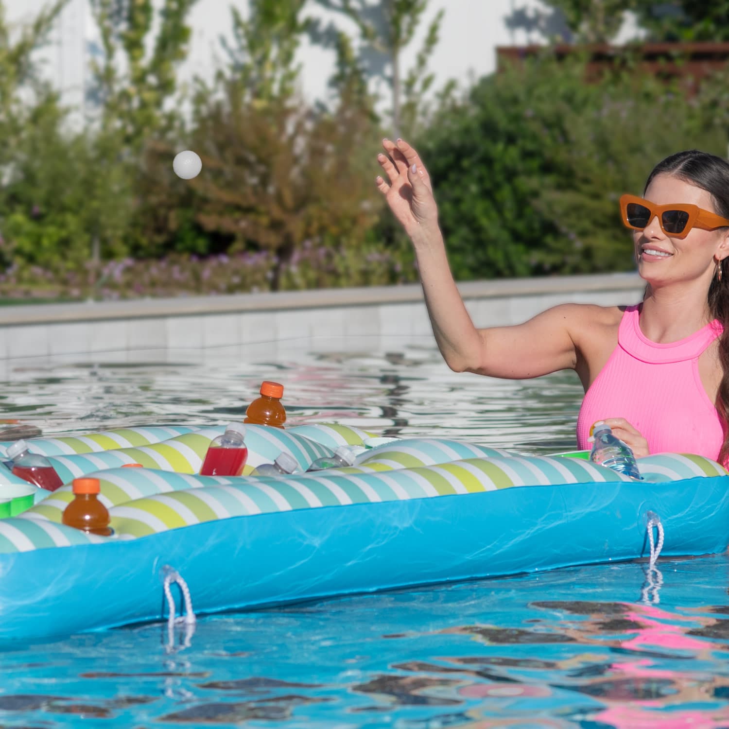 Woman in pink swimsuit and sunglasses on a colorful inflatable raft in a pool.