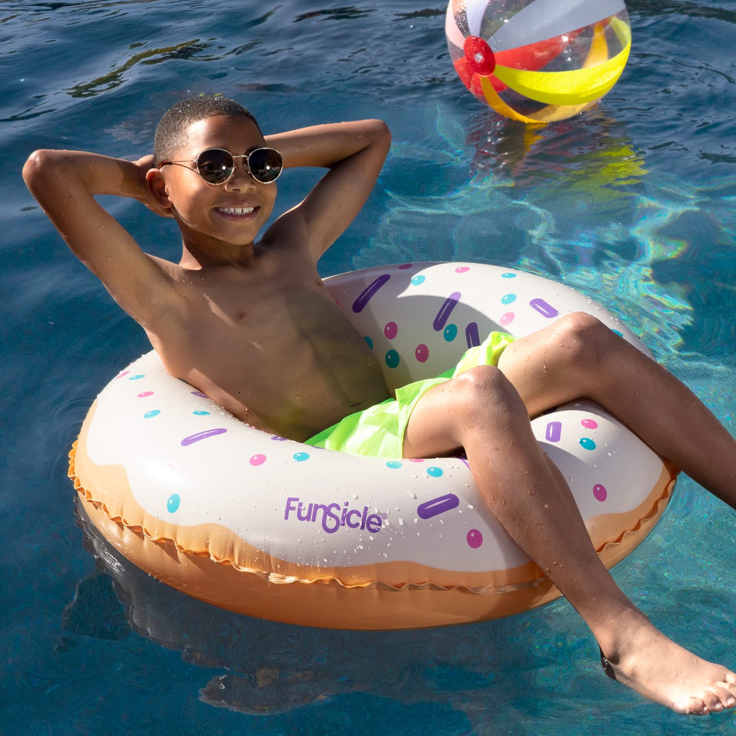 Child on a donut-shaped inflatable tube in a pool with a colorful ball in the background