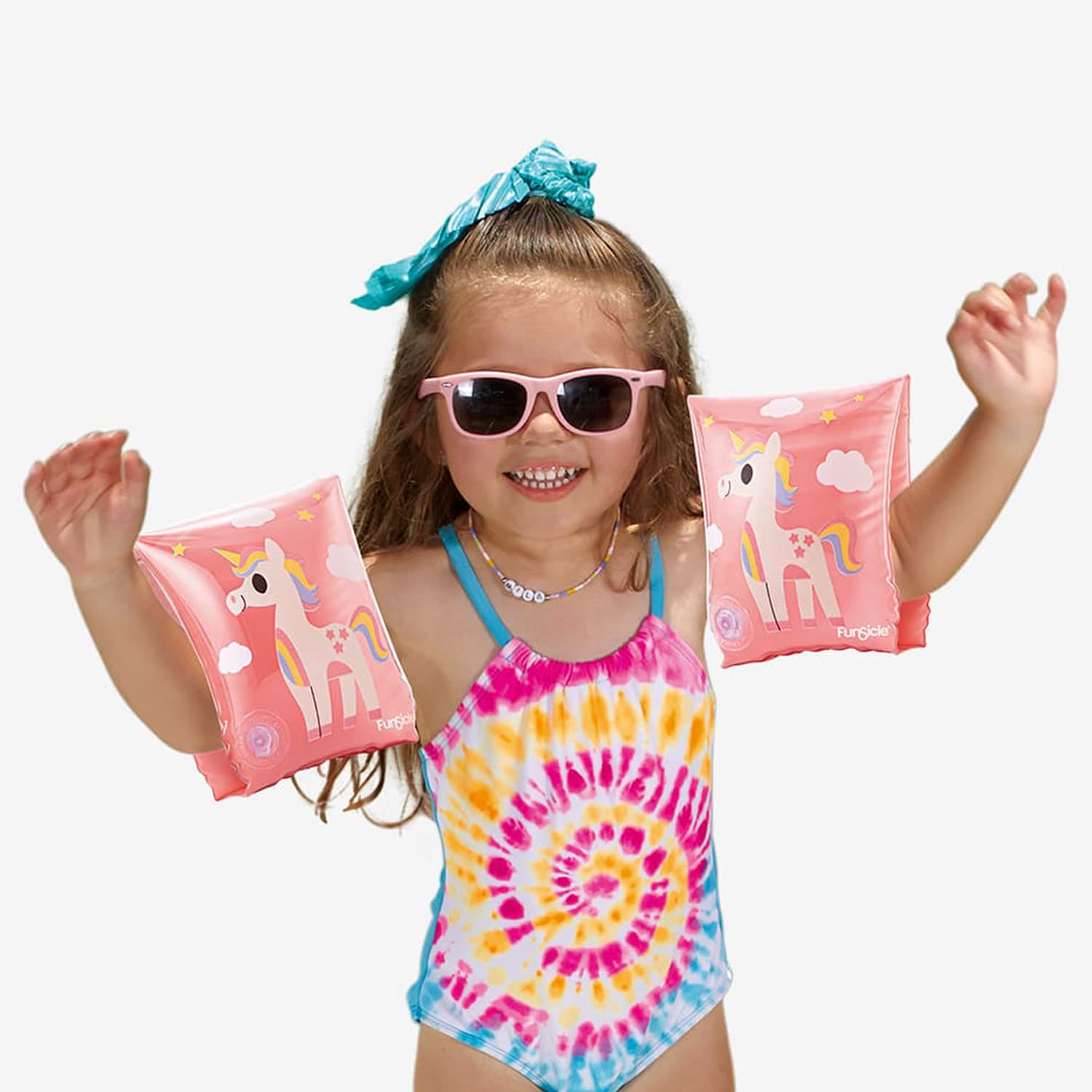 Child wearing pink unicorn arm floats, sunglasses, and a tie-dye swimsuit on a white background