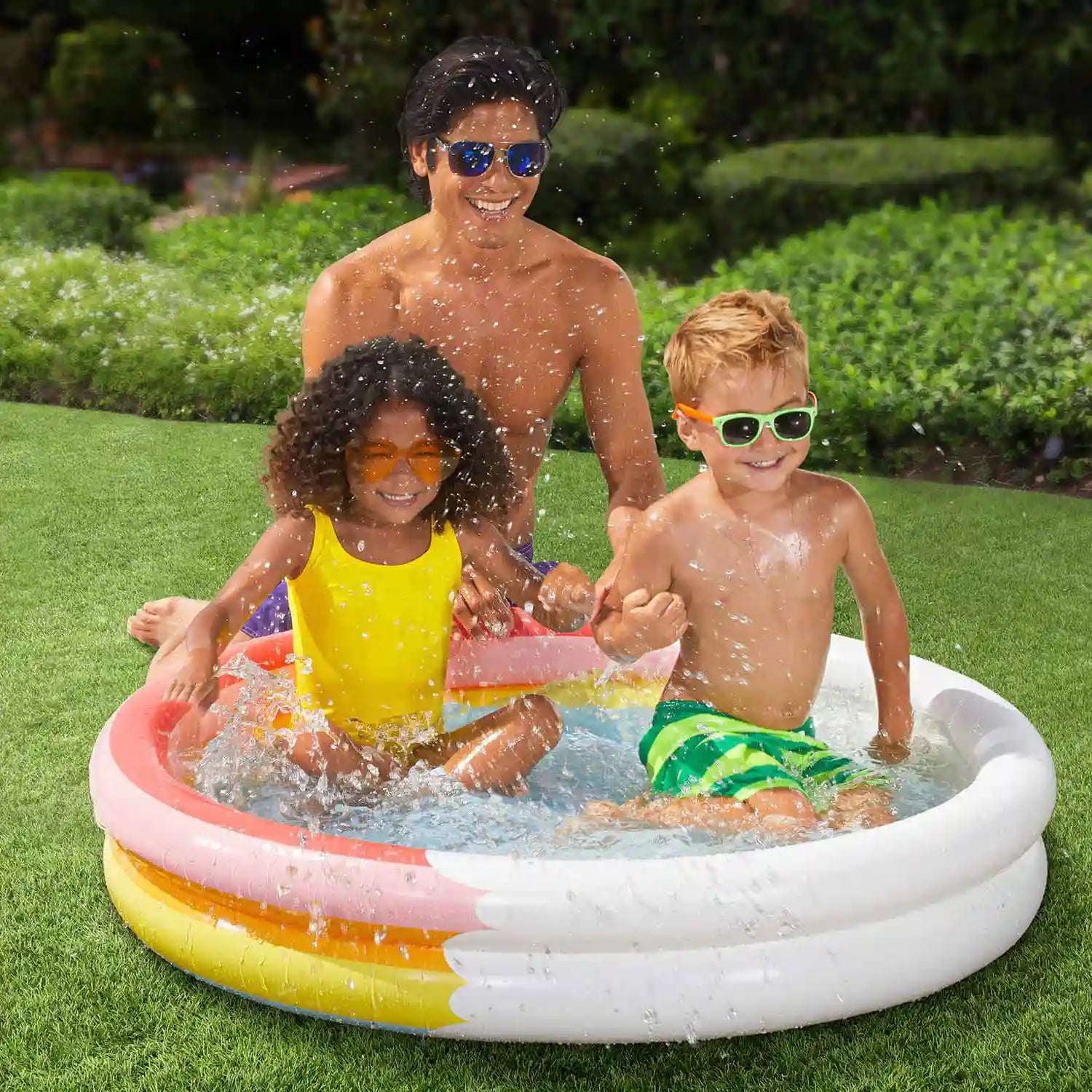 Father sits next to 2 kids inside Funsicle Rainbow Heaven FunRing Pool on grass