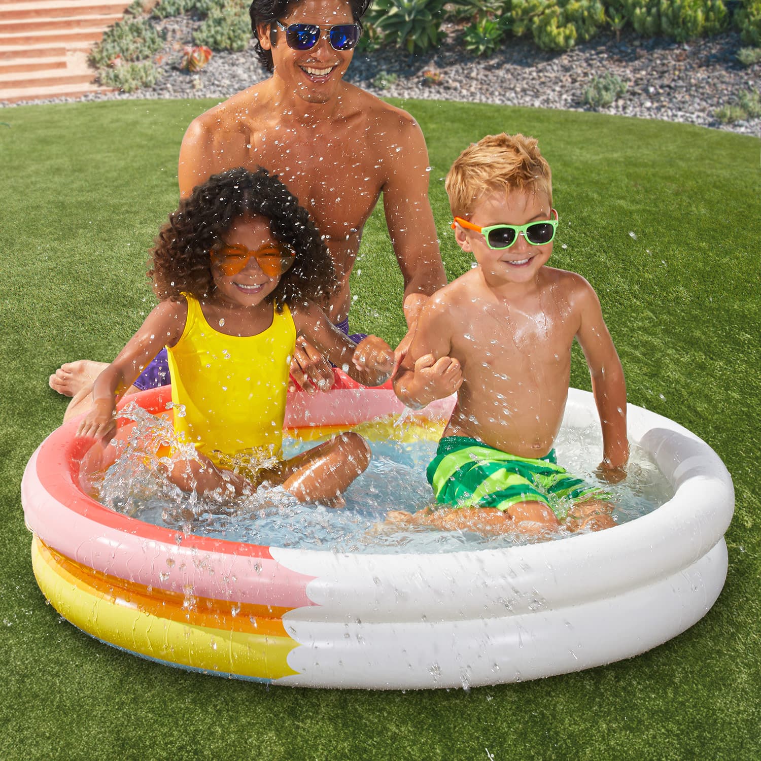 Father sits next to 2 kids inside Funsicle Rainbow Heaven FunRing Pool on grass