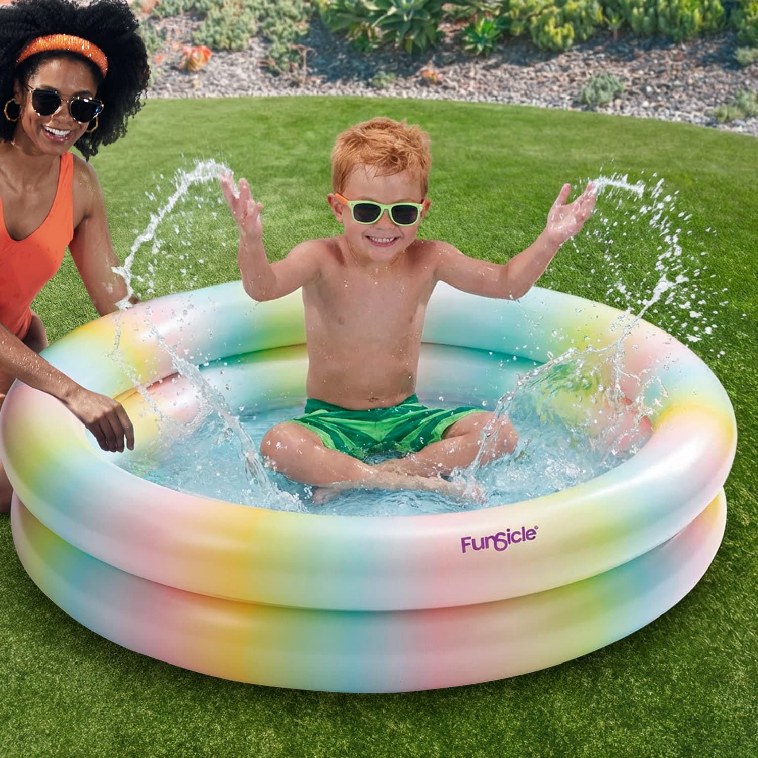 Child playing in a colorful inflatable pool with a woman nearby on a grassy area.