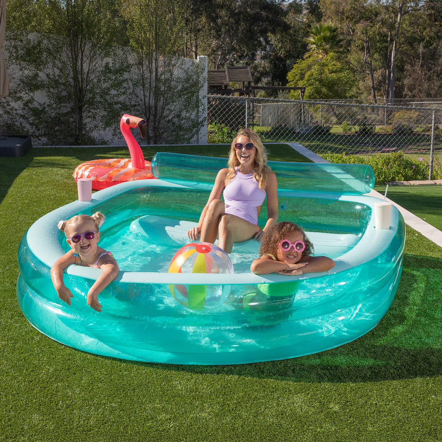 Inflatable pool with children and a flamingo floatie on a grassy area.