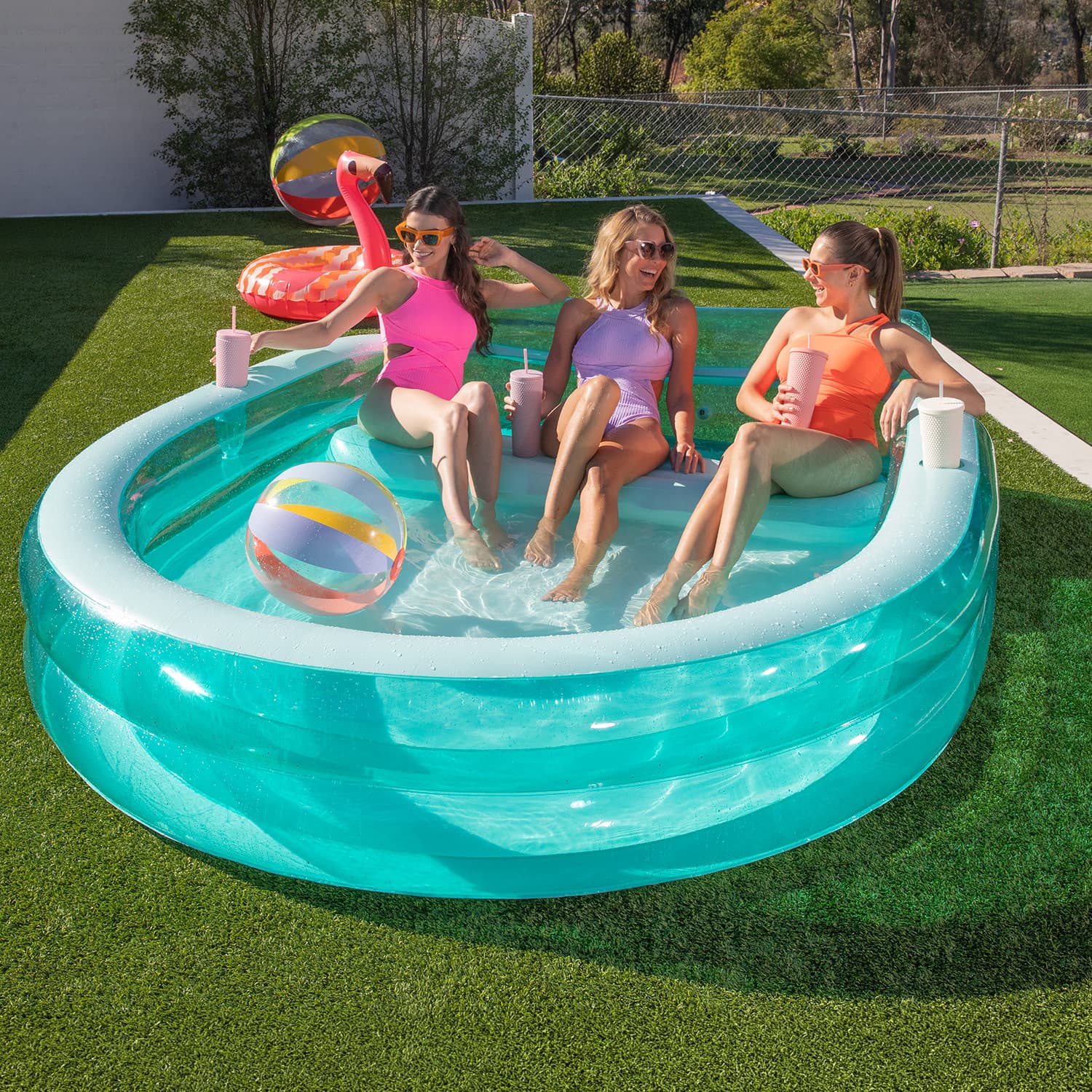 Three women sitting in a small inflatable pool on a sunny day.