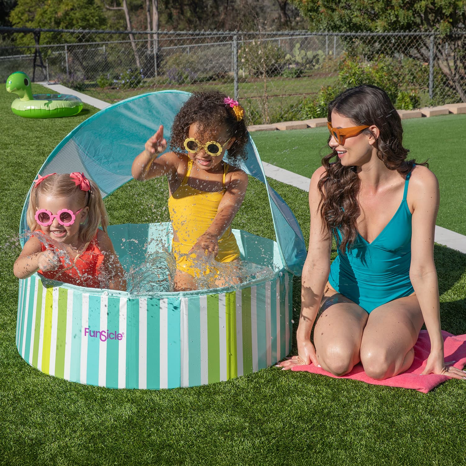 Two children playing in a striped pool with a woman supervising, all outdoors on grass.